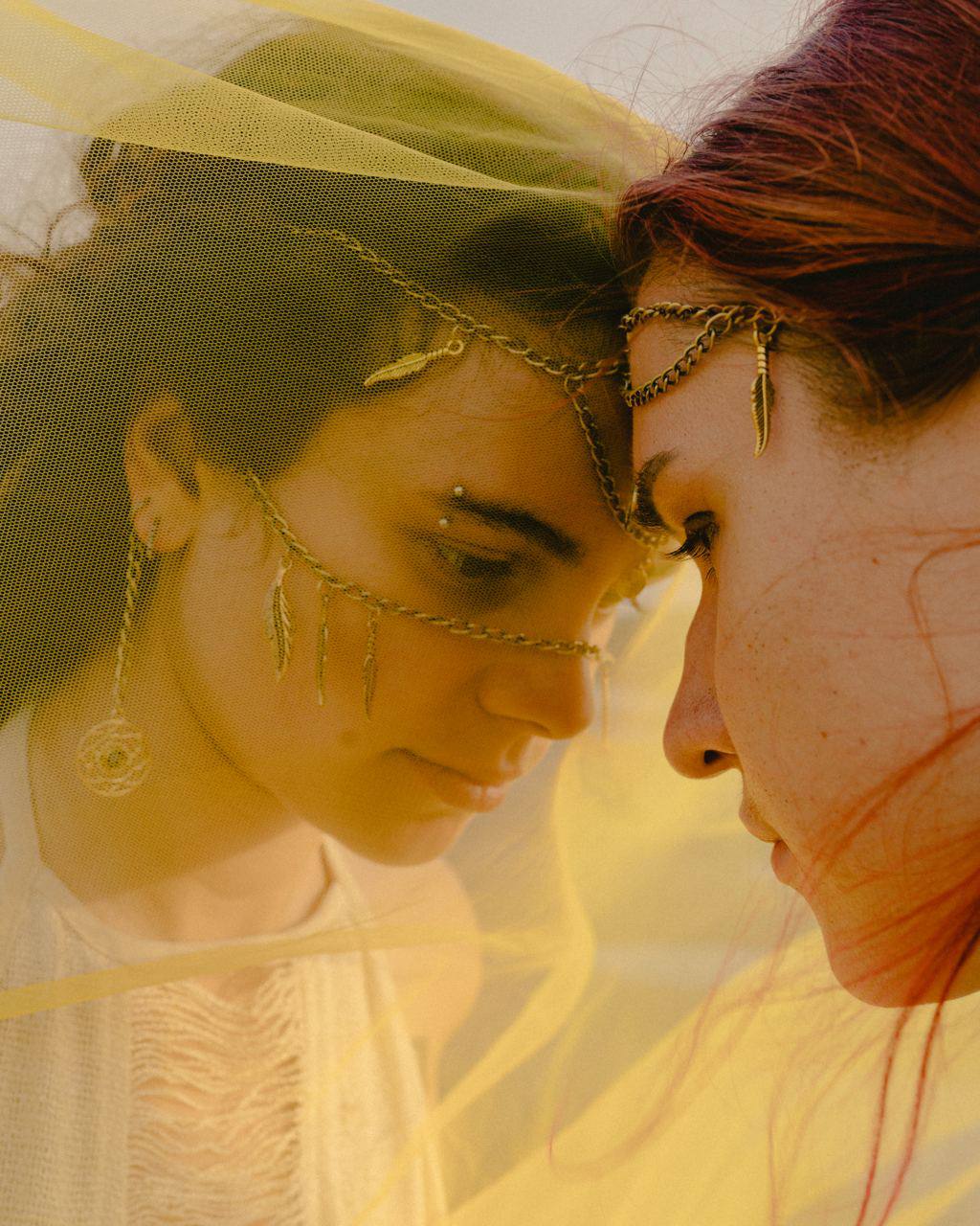 Intimate portrait of two women with gold headchains in gentle embrace